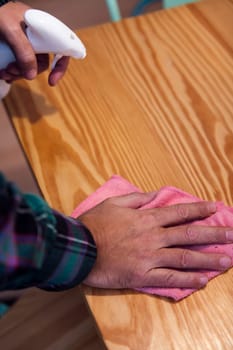 closeup of the hands of a person cleaning a wooden table with a rag and a spray, home cleaning concept, copy space for text