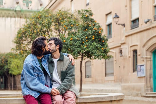happy young couple of gay men kissing tenderly holding hands, concept of urban lifestyle and love between people of the same sex, copy space for text