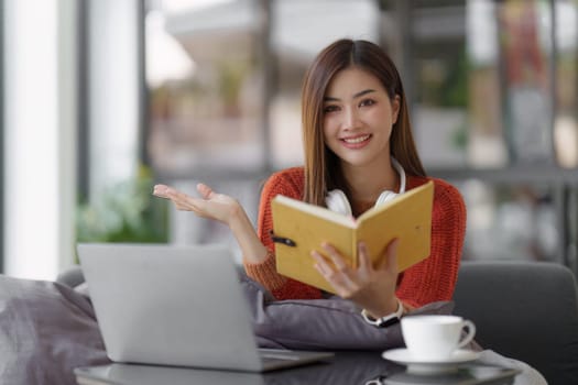 Beautiful Asian Woman smile and relaxing at home and using laptop computer sitting on cozy sofa.