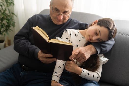 Happy little girl with grandfather reading story book at home.