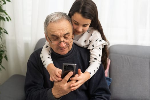 Senior man 60-65 years old showing his little granddaughter how to use a smartphone.