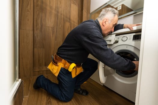 an elderly man repairs a washing machine.