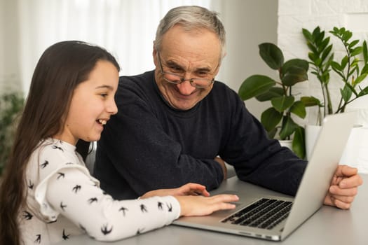 Happy retirement grandfather and pretty granddaughter laughing while watching e-book for learning to education together by laptop. Family educational at home concept. Technology and education