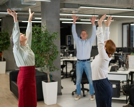 Four office workers warm up during a break. Employees do fitness exercises at the workplace