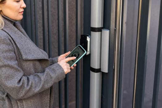 woman standing near the door and locking it with online application on her smartphone.