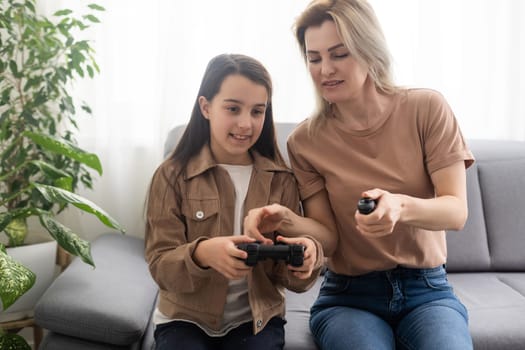 good relationship cute little girl with young mother using joystick playing video game sitting together in living room wooden floor enjoying family holiday.