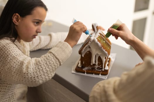 Mother and daughter making gingerbread cookies house, decorating at home, Christmas concept.