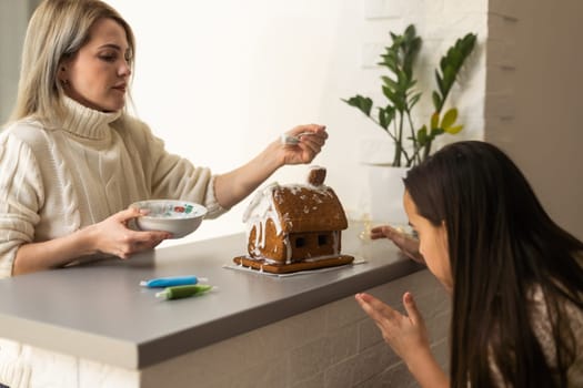 Mother and daughter making gingerbread cookies house, decorating at home, Christmas concept.