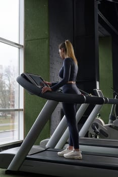 Beautiful muscular woman on a treadmill. wearing blue leggins and long sleeve top. setting up running program