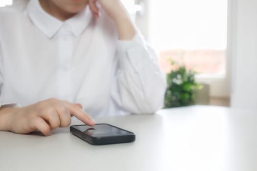 Hands of young woman using online app on mobile phone, making call, browsing Internet, chatting on social media, holding cellphone, texting, typing message. Close up on white desk bright colors scrolling