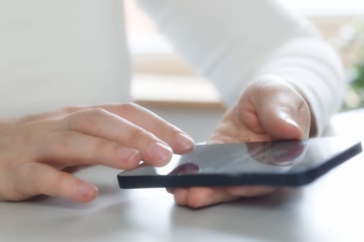 Hands of young woman using online app on mobile phone, making call, browsing Internet, chatting on social media, holding cellphone, texting, typing message. Close up on white desk bright colors scrolling