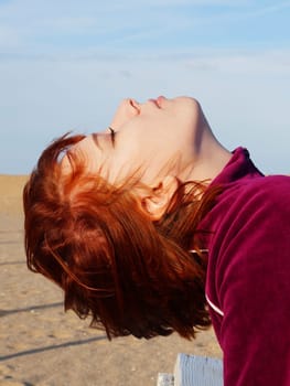 Portrait of a red-haired teenage girl with closed eyes on an empty beach.