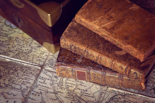 Pile of antique books with a leather cover and golden ornaments, close to a wooden box on an ancient topographic map