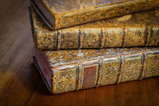 Pile of antique books with a leather cover and golden ornaments on a wooden table