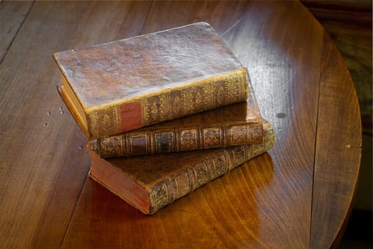 Pile of antique books with a leather cover and golden ornaments on a wooden table