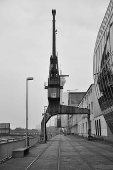 Vertical grayscale shot of an old cargo crane in the Media Harbor in Dusseldorf, Germany.