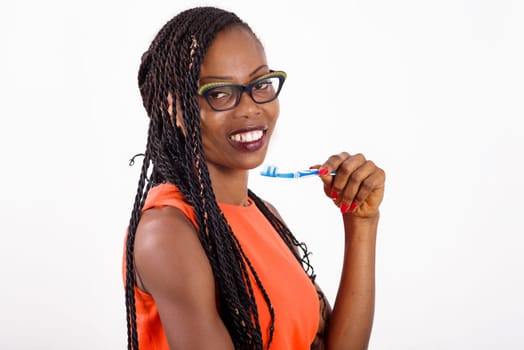 young girl standing in eyeglasses on white background smiling and holding toothbrush under chin.