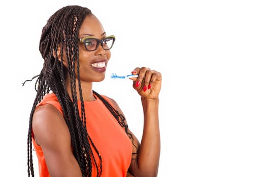 young girl standing in eyeglasses on white background smiling to hold toothbrush to chin.