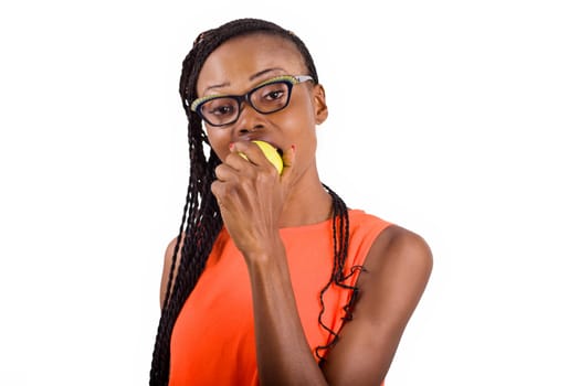 young girl standing in glasses on white background eating an apple while looking at the camera.