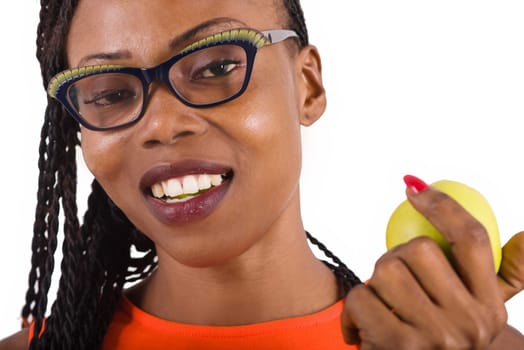 young girl standing in glasses on white background eating an apple while looking at the camera.