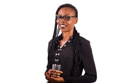 young woman standing on white background in eyeglasses to look at the camera smiling with glass of water in hand.