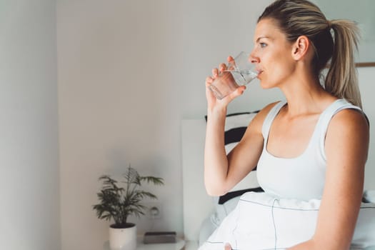 Smiling young caucasian woman taking her morning supplements, vitamin pills with a glass of water at home. High quality photo