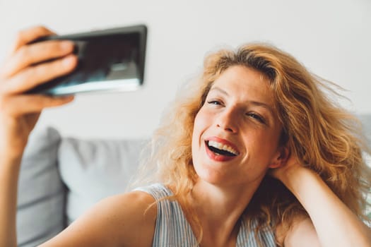 Cheerful happy caucasian woman relaxing at home on her day off work. Adult content woman spending time at home, in her apartment, resting on the couch, having a cup of coffee, feeling good.