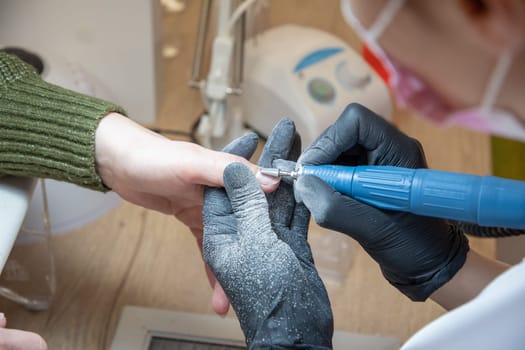 The manicurist grinds off the old coating from the client's nails with the help of a professional electric nail file. High quality photo