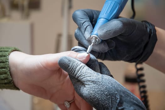 The manicurist grinds off the old coating from the client's nails with the help of a professional electric nail file. High quality photo