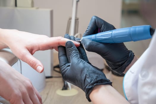 The manicurist grinds off the old coating from the client's nails with the help of a professional electric nail file. High quality photo