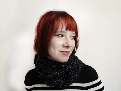 portrait of a smiling red-haired teenage girl in a black scarf on a white background.