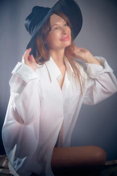 Portrait of a young sexy girl in white shirt and hat on a grey background. Classic style. dramatic portrait