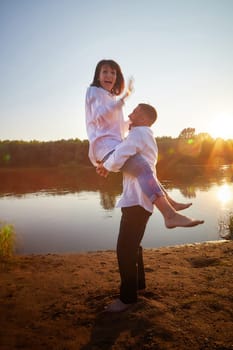 Happy Couple relaxin, having fun and hug on nature near water of river or lake in summer sunny evening during sunset. Family or lovers have date and rest outdoors. Concept of love and friendship