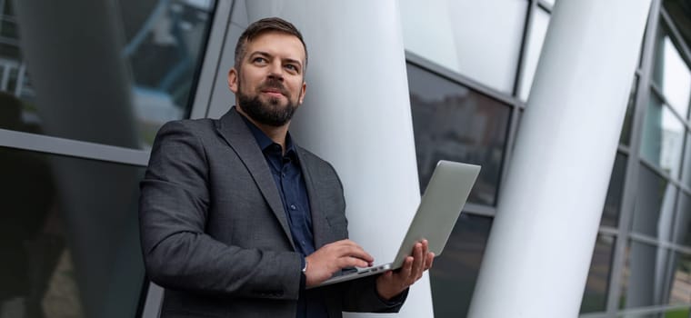 pensive male architect with a laptop works on the background of the building.