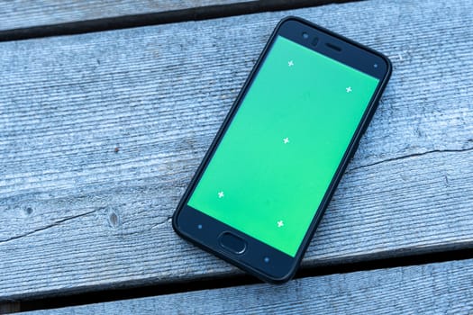 a smartphone with a green screen lies on a faded wooden background. chromakey, mockup. mobile phone app advertising