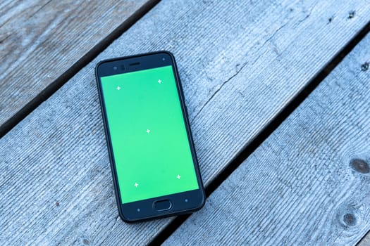 a smartphone with a green screen lies on a faded wooden background. chromakey, mockup. mobile phone app advertising