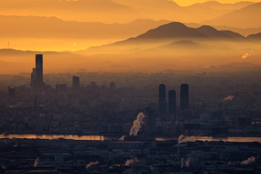 Orange haze from industrial emissions in city by river and mountains at sunrise. High quality photo