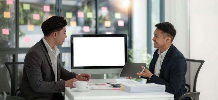 Two business people talk project strategy at office meeting room. Businessman discuss project planning with colleague at modern workplace while having conversation and advice on financial data report