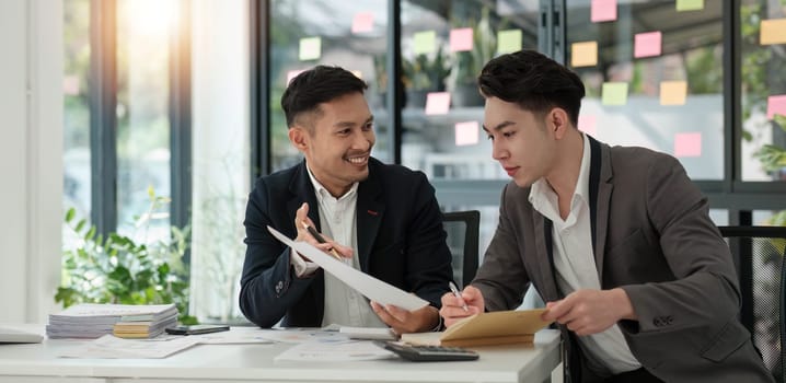 Two business people talk project strategy at office meeting room. Businessman discuss project planning with colleague at modern workplace while having conversation and advice on financial data report