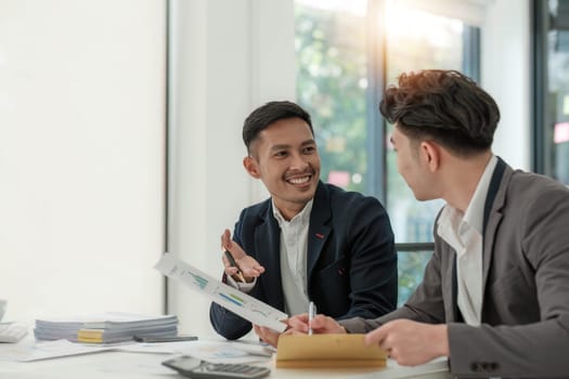 Two business people talk project strategy at office meeting room. Businessman discuss project planning with colleague at modern workplace while having conversation and advice on financial data report