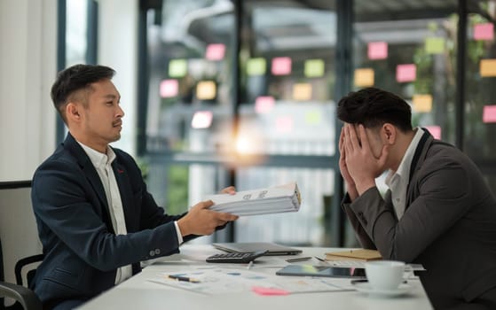 Sad and stressed Asian male office worker or businessman receives a complaint from his boss while working on his project with his team.