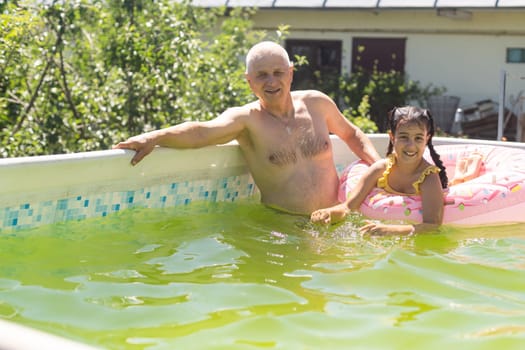 grandfather and granddaughter swimming in the pool in the garden near the house.