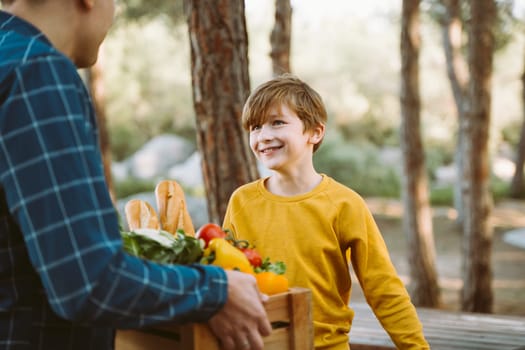 Father and son farmers holding a wooden crate with supplies groceries. Man male dad and his should kid boy child delivered a framed box with organic vegetables and bread to farmers market