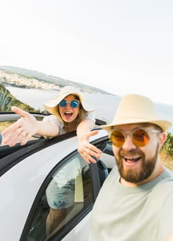 Happy beautiful couple in love taking a selfie portrait driving a convertible car on the road at vacation. Rental cars and vacation concept