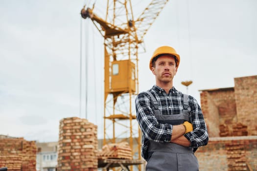 With arms crossed. Construction worker in uniform and safety equipment have job on building.