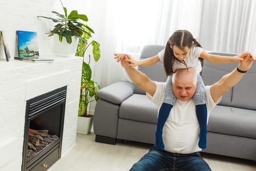 Cute little girl spending time with positive active grandpa in living room.