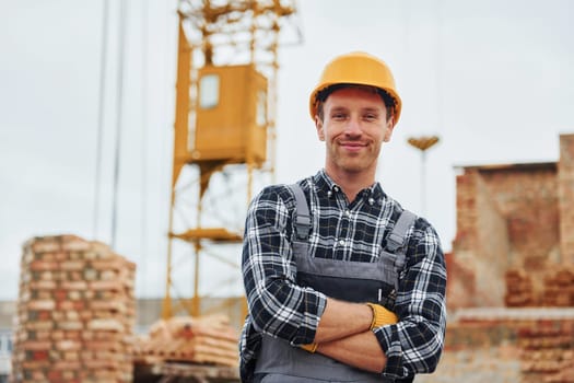 With arms crossed. Construction worker in uniform and safety equipment have job on building.