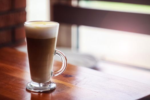Large glass cup of coffee on a wooden table by the window, copy space