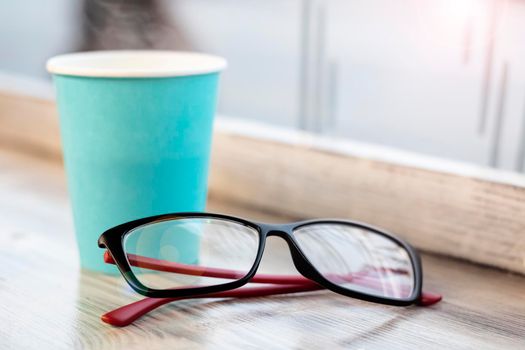 Blue paper cup with coffee and glasses on a wooden table