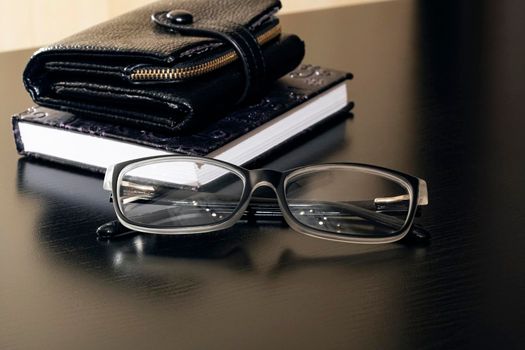 Glasses, wallet and notebook on a wooden table close up